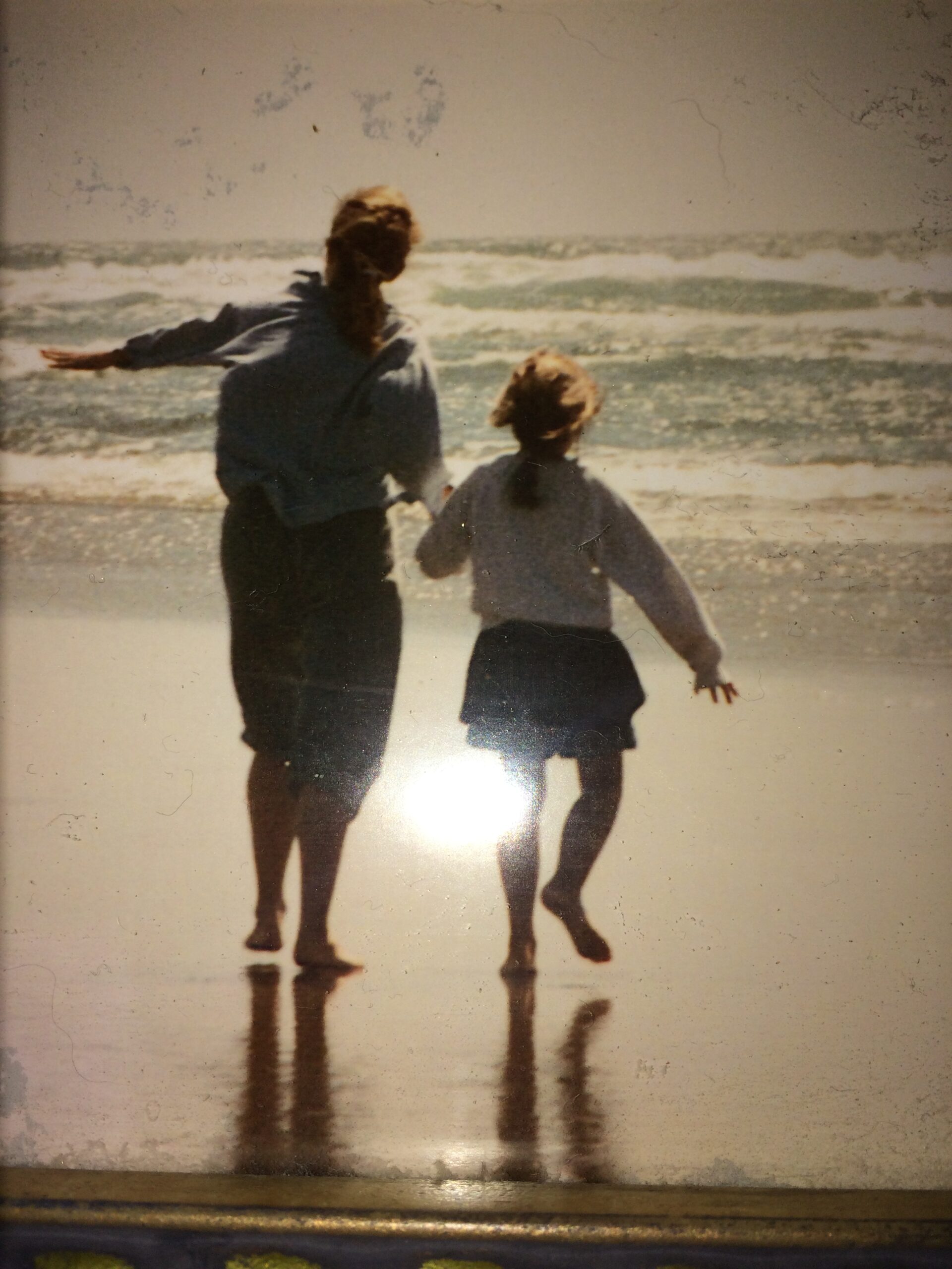 A woman and a girl walk hand-in-hand along the beach